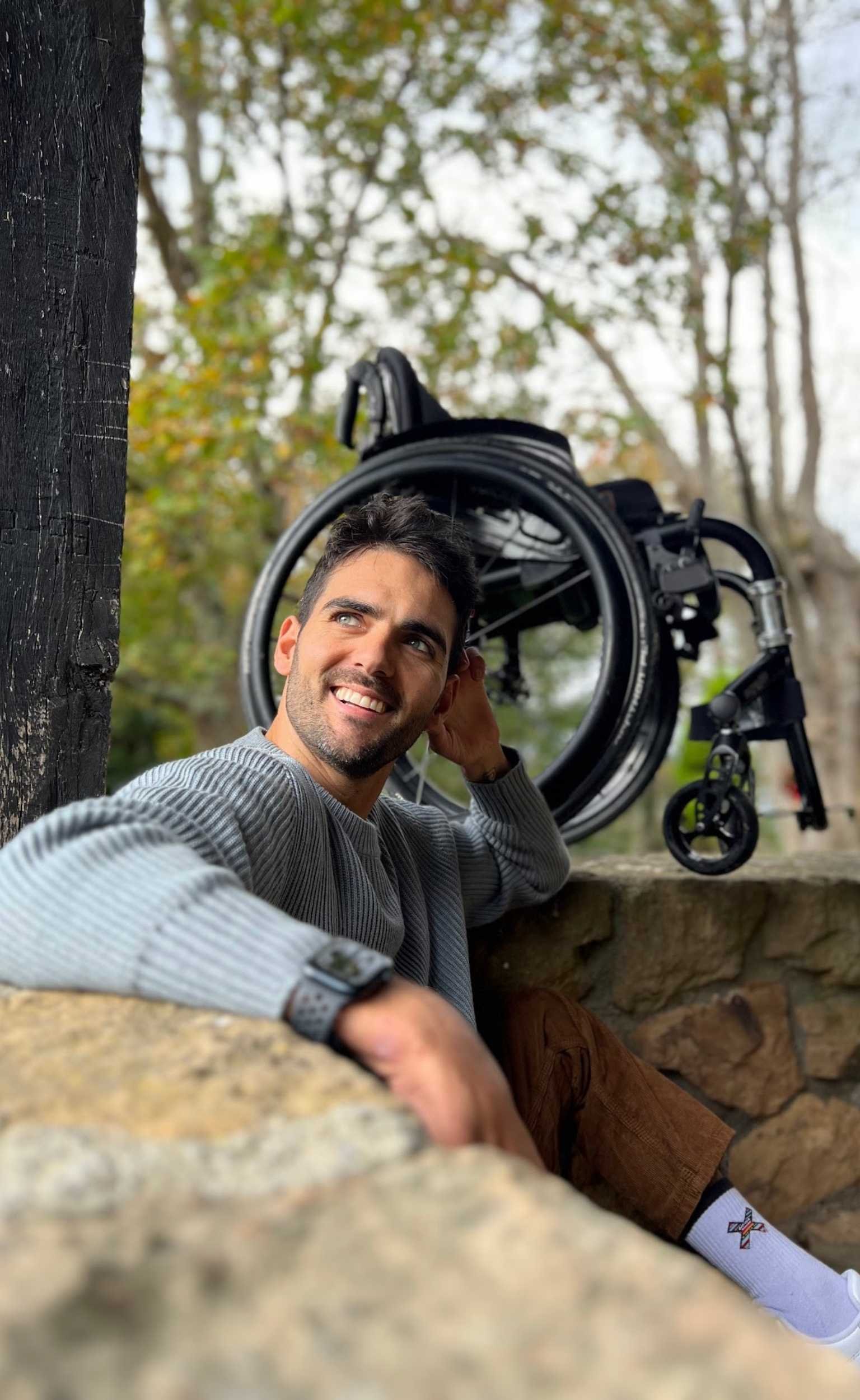 Ander sentado en un muro de piedra, con su silla de ruedas detrás